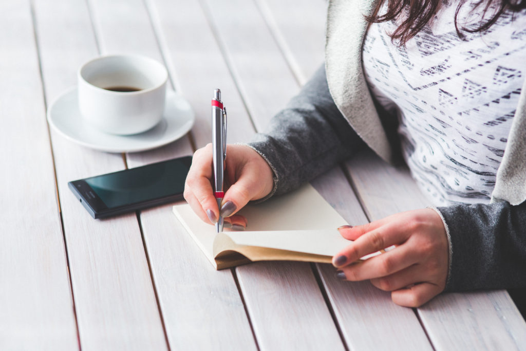 seo checklist; woman writing on notepad with coffee and smartphone