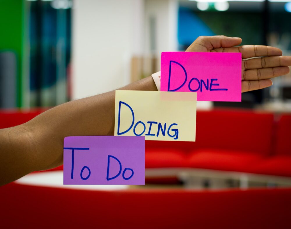 Three big sticky notes appear on an outstretched arm in ascending order that say, "To Do," "Doing," and "Done."