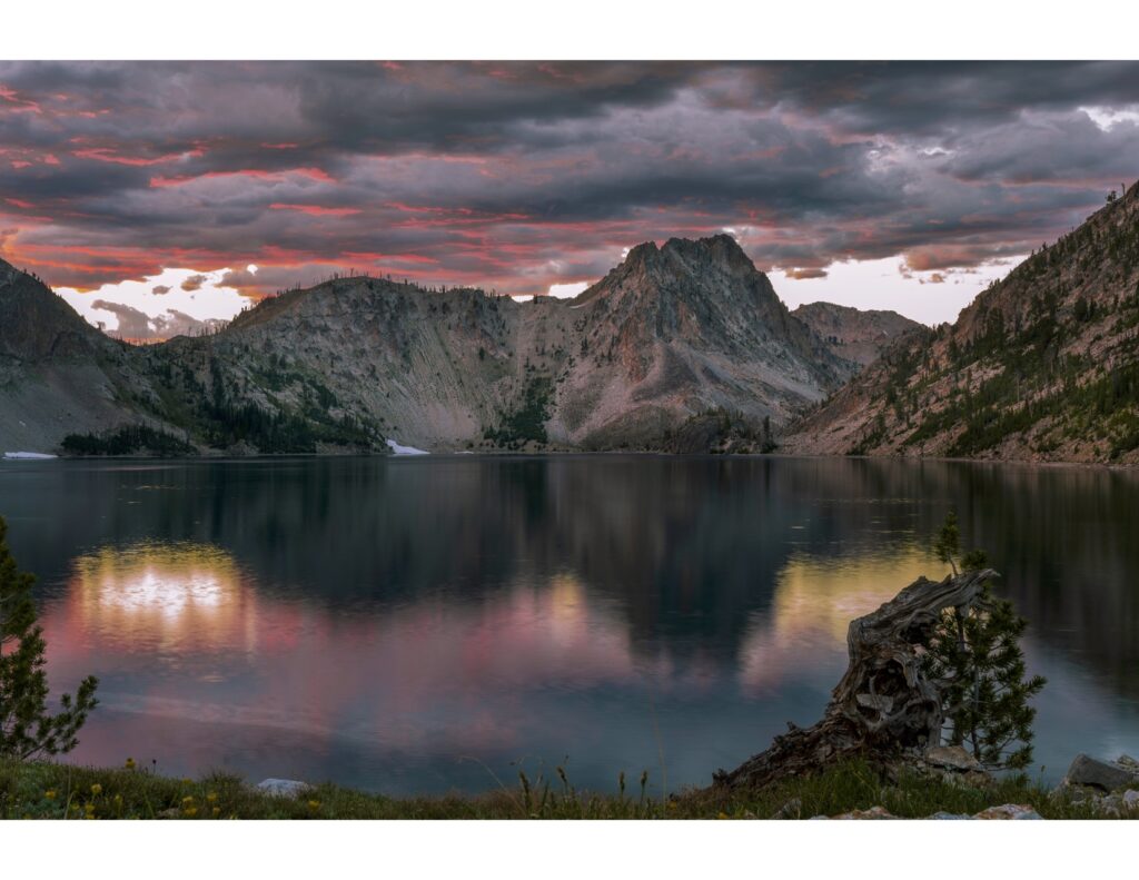 Sun setting behind mountain range with a colorful reflection on the water. 