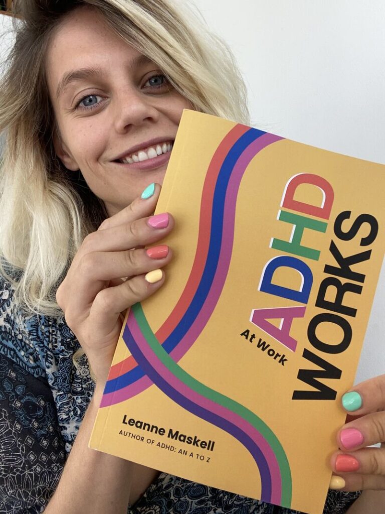 Leanne Maskell, a white woman with cascading blonde hair & blue eyes, holds her book, "ADHD at Work Works" while smiling.